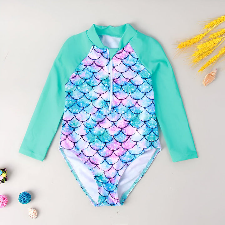 Maillot de bain une pièce pour enfant, manches longues turquoise, corps blanc et motifs écailles de sirène colorées sur les côtés. Idéal pour la plage ou la piscine.