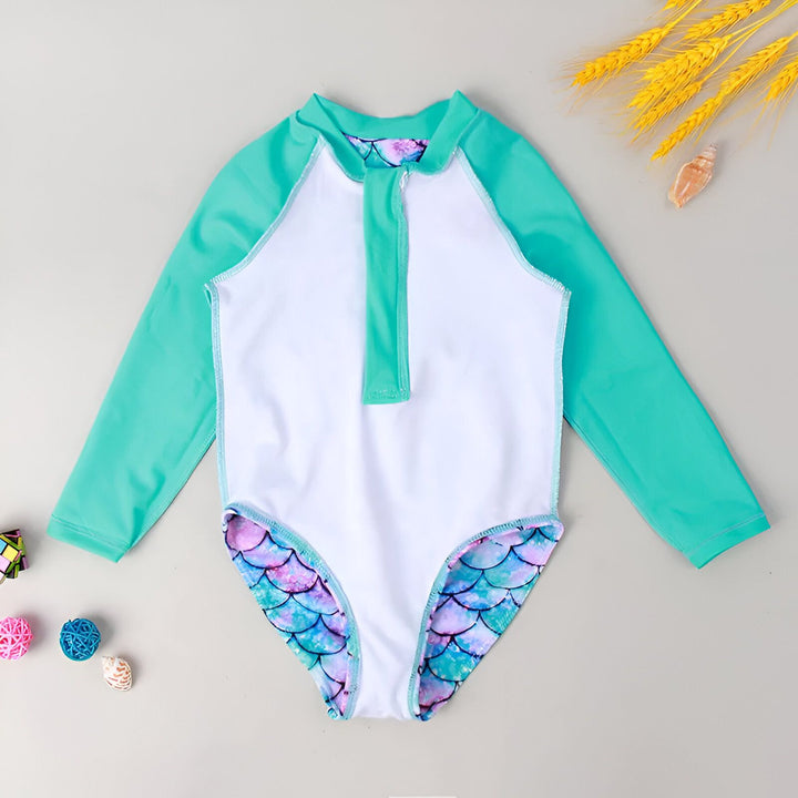 Maillot de bain une pièce manches longues pour enfant. Imprimé écailles de sirène multicolores (bleu, rose, violet). Fermeture éclair devant, manches vert d'eau. Accessoires de plage décoratifs.