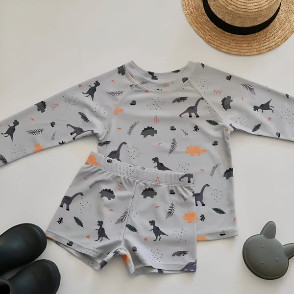 Ensemble de bain enfant avec motif dinosaures, comprenant un haut à manches longues et un short. Accessoires : chapeau de paille, bottes de pluie et jouet en forme de lapin. Idéal pour la plage ou la piscine.