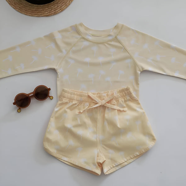 Un jeune enfant avec des lunettes de soleil et un maillot de bain à motifs de dinosaures, posant avec un canard gonflable près d'une piscine carrelée en bleu. Prêt pour l'été et les jeux aquatiques.