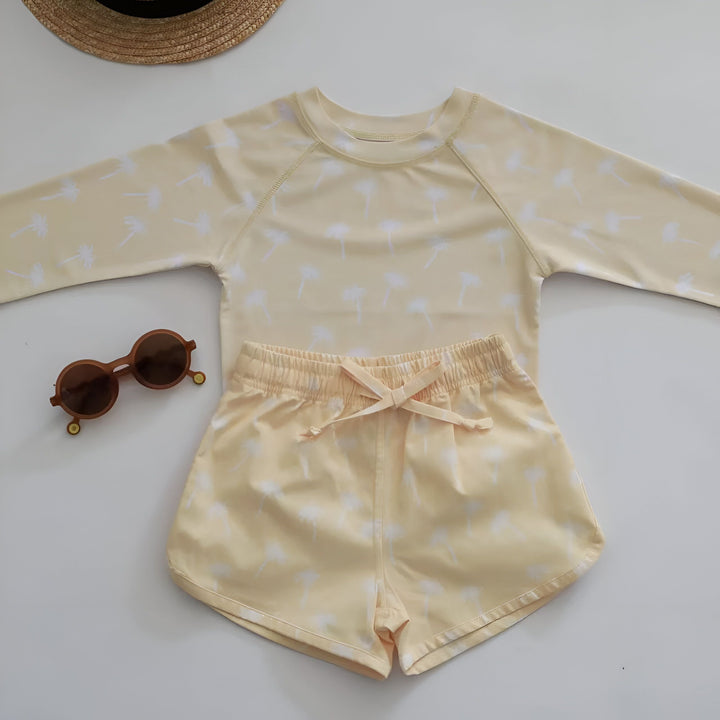 Un jeune enfant avec des lunettes de soleil et un maillot de bain à motifs de dinosaures, posant avec un canard gonflable près d'une piscine carrelée en bleu. Prêt pour l'été et les jeux aquatiques.