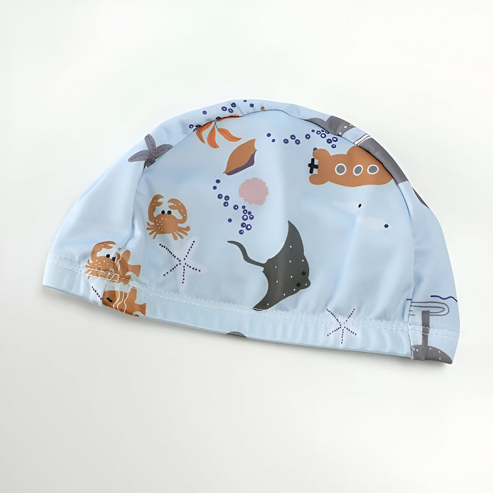 Motifs marins sur tissu bleu : raie manta, étoile de mer, ours marron, et motifs abstraits ronds. Tissu texturé avec un motif répétitif délicat. Idéal pour chambre d'enfant ou décoration thématique maritime.