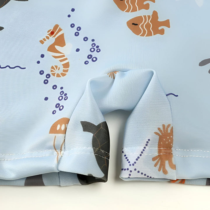 Détail du col zippé d'un maillot de bain bleu clair imprimé avec des motifs de créatures marines : baleines, pieuvres et méduses. Idéal pour la plage ou la piscine.