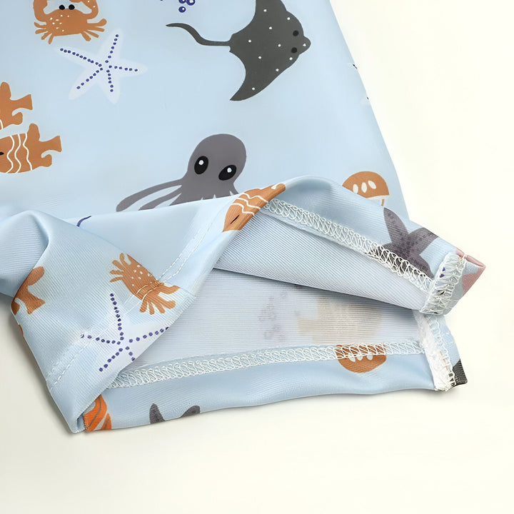 Manche d'un vêtement bleu clair avec motifs marins : dauphin gris, raie noire, méduse orange, crabe, hippocampe et bulles bleues. Idéal pour la plage et la natation.
