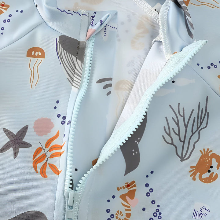 Fermeture éclair ouverte sur un maillot de bain bleu clair imprimé animaux marins : baleine, étoile de mer, méduse, crabe et hippocampe. Motif marin enfantin pour la plage ou la piscine.