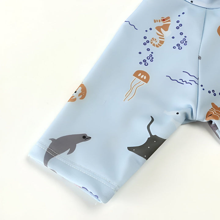 Motif marin bleu pastel sur tissu : étoiles de mer, poulpe, poisson clown, raie manta et crabe. Détail de couture blanche. Idéal pour enfants, thème océanique, et articles de plage.