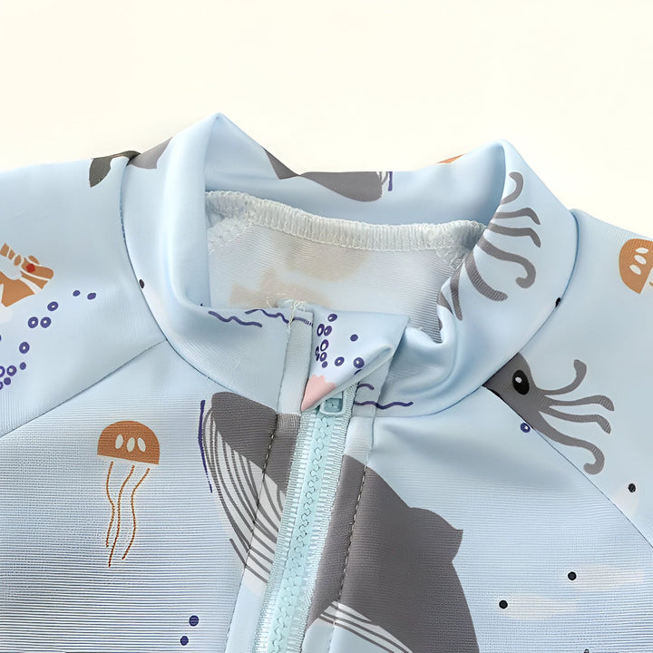 Motif marin sur tissu bleu clair : hippocampe, poissons, méduse, tortue. Impression de créatures marines et bulles violettes. Texture du tissu visible avec des plis. Design aquatique pour vêtements ou décoration.