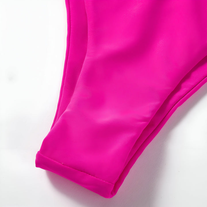 Maillot de bain deux pièces rose vif avec soutien-gorge à armatures et culotte échancrée, posé sur un fond en bois clair. Style moderne et estival.