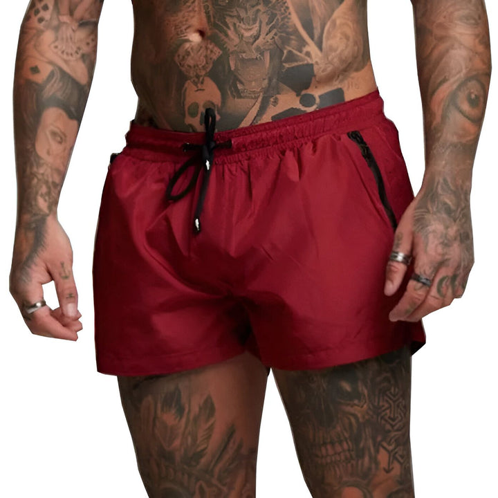 Homme de dos en short de bain jaune, avec des tatouages sur les bras. Idéal pour la plage ou la piscine. Mode estivale et style décontracté.
