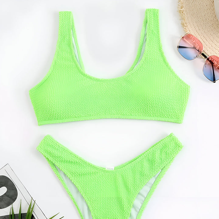 Vue de dessus d'un ensemble de bikini texturé vert menthe, avec un chapeau de paille et des lunettes de soleil roses/bleues. Accessoires de plage pour l'été.