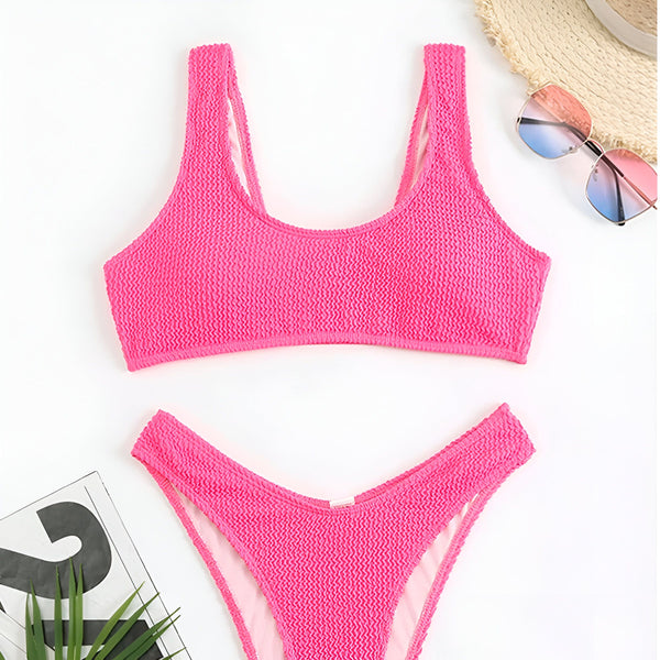 Image d'un ensemble de bikini texturé orange vif, avec un haut de soutien-gorge et une culotte assortie, posé sur un fond blanc avec des accessoires d'été tels qu'un chapeau de paille et des lunettes de soleil.