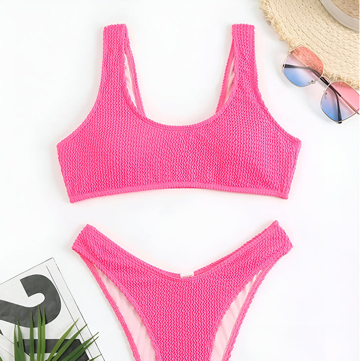 Image d'un ensemble de bikini texturé orange vif, avec un haut de soutien-gorge et une culotte assortie, posé sur un fond blanc avec des accessoires d'été tels qu'un chapeau de paille et des lunettes de soleil.