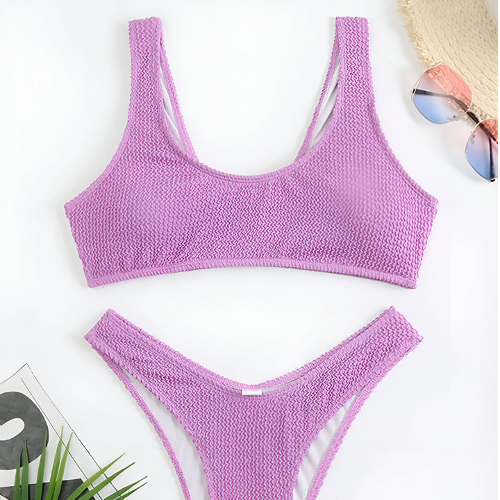 Maillot de bain deux pièces rose vif texturé, avec un chapeau de paille, des lunettes de soleil et un magazine, sur un fond blanc. Ensemble d'été pour la plage ou la piscine.