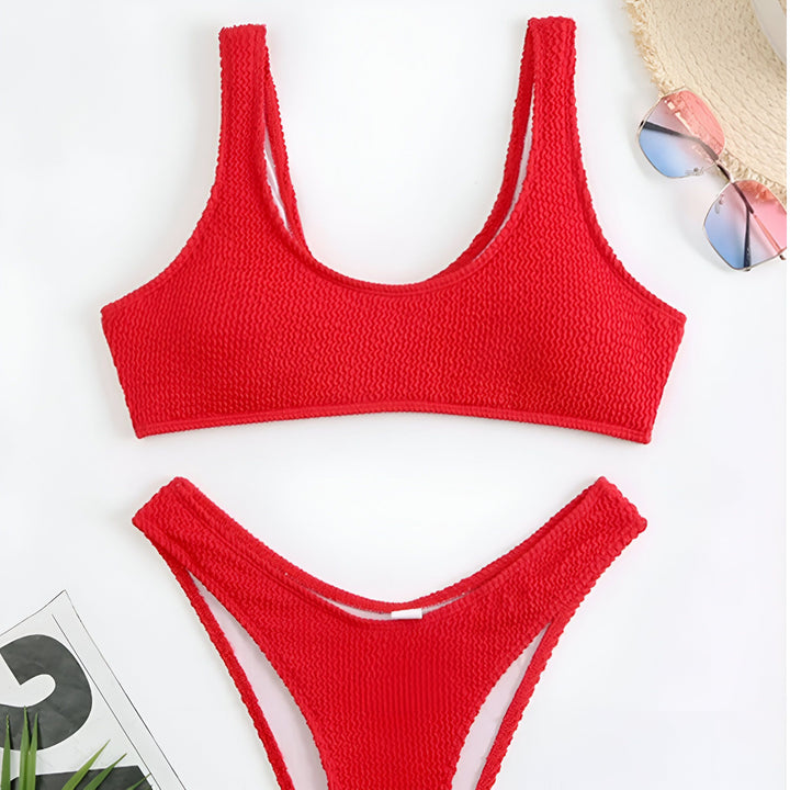 Gros plan d'une femme portant un bikini vert texturé. Le maillot de bain est lumineux et met en valeur son teint bronzé. Elle est en extérieur, devant un mur clair.