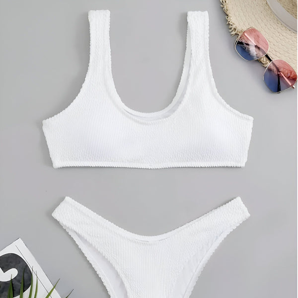 Maillot de bain deux pièces noir texturé, vue de dessus. Chapeau de paille et lunettes de soleil roses et bleues à droite. Élégance estivale et prêt pour la plage.