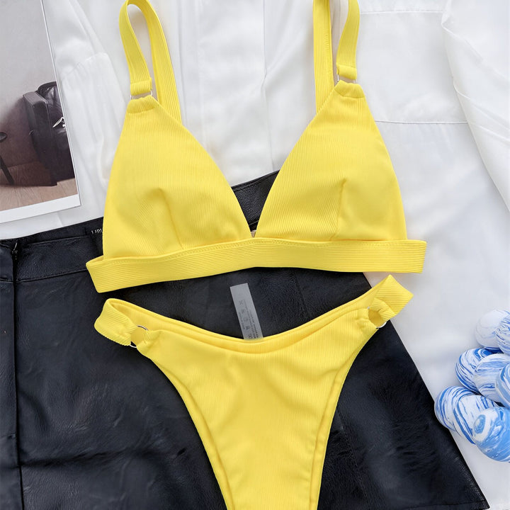 Image d'une femme portant un bikini noir texturé avec des anneaux dorés, partiellement recouverte d'un blazer blanc. Mode plage, vêtements d'été, maillot de bain élégant, tenue estivale féminine.