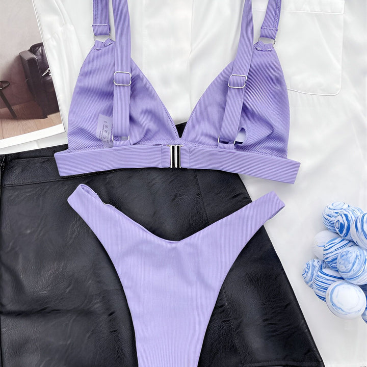 Femme portant un bikini rose vif avec des anneaux dorés, partiellement cachée derrière une veste de costume blanche. Vêtement de plage tendance et estival.