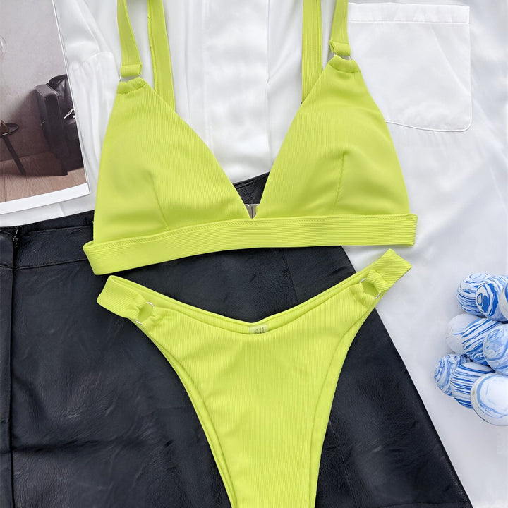 Gros plan d'une femme portant un bikini jaune vif et un blazer blanc. Le bikini est composé d'un haut triangle et d'une culotte assortie, accentués d'anneaux métalliques. Le blazer blanc ajoute une touche élégante à l'ensemble estival.