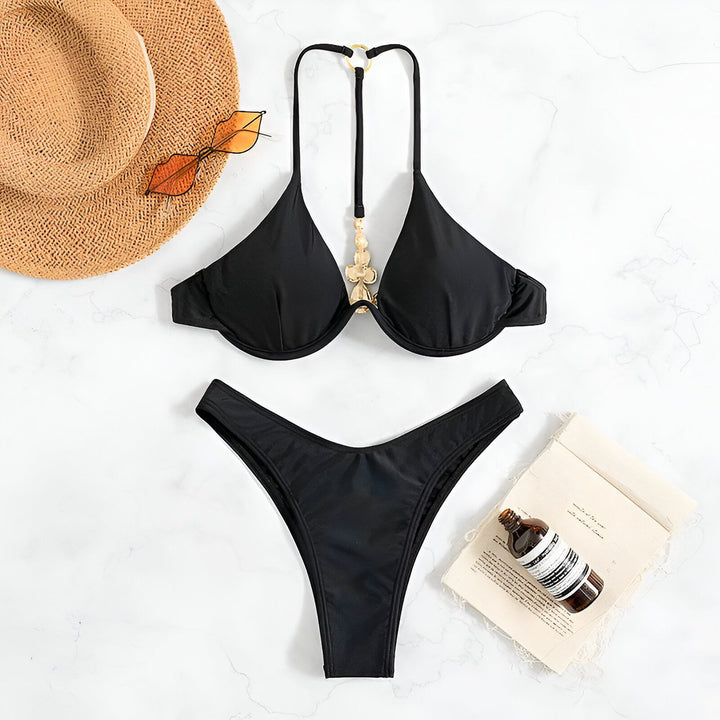 Ensemble de bikini noir sur une surface en marbre avec un chapeau de paille, des lunettes de soleil originales, un livre et une bouteille d'huile corporelle, créant une ambiance estivale.