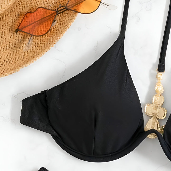 Gros plan d'un soutien-gorge de bikini noir, chapeau de paille et lunettes orange sur fond blanc. Accessoires de mode estivale.