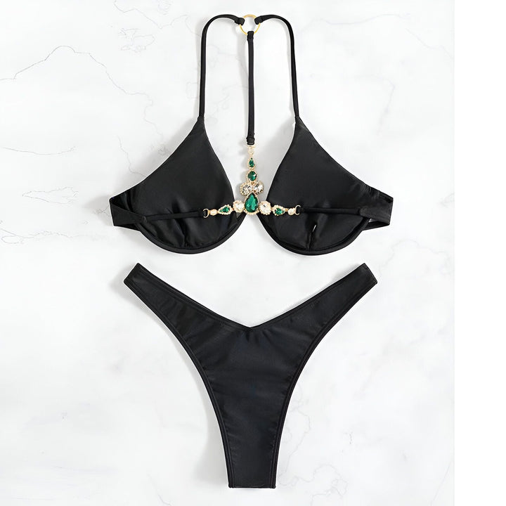 Culotte de bikini noire avec détails de couture, posée sur un fond en marbre avec un livre ouvert et un flacon. Accessoire de mode estival.
