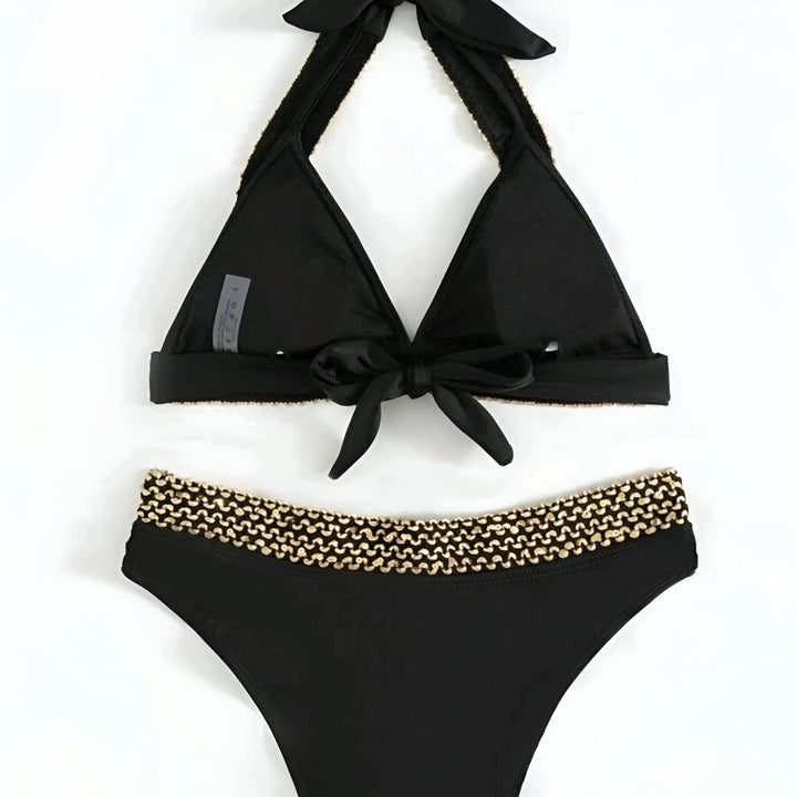 Image d'un bikini noir avec des détails beiges, accompagné de lunettes de soleil et d'un chapeau de paille, idéal pour la plage ou la piscine.