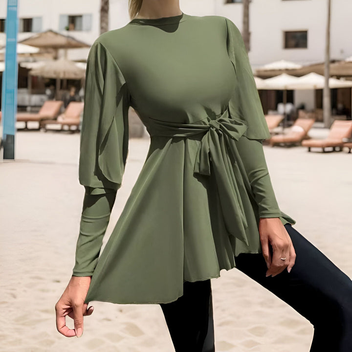 Femme portant un burkini vert olive avec manches larges et un turban assorti. Le burkini a une ceinture nouée à la taille. Bas noir.