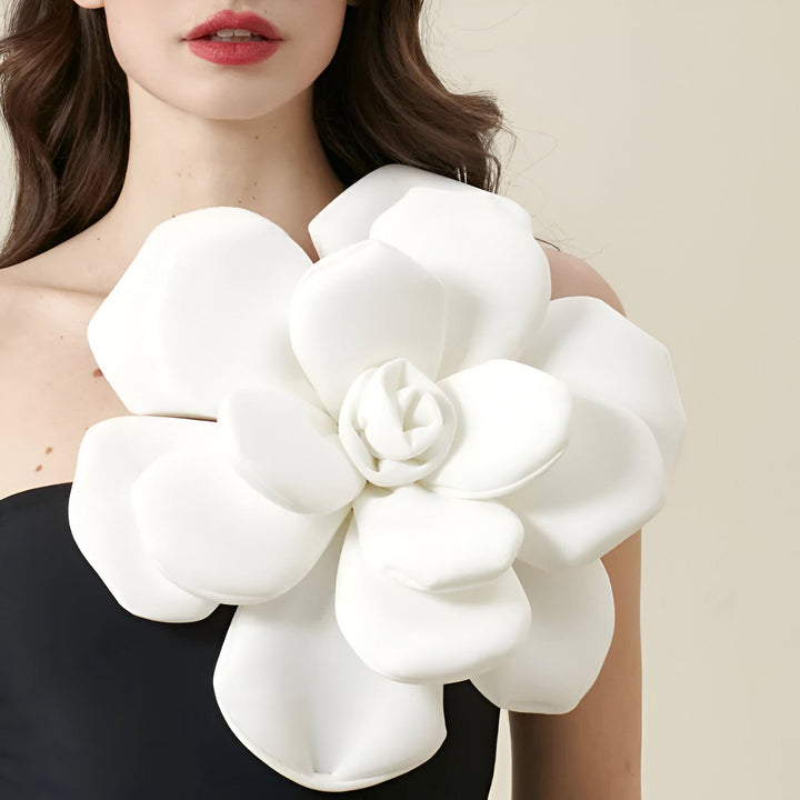 Portrait d'une femme portant un maillot de bain noir asymétrique orné d'une grande fleur blanche. Élégance et style estival.