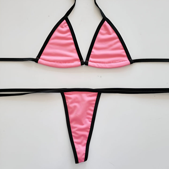 Ensemble de bikini rose et noir sur fond blanc. Haut triangle et bas string. Mode été, maillot de bain pour femme.