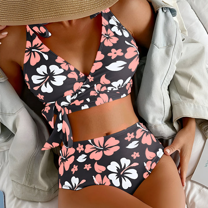 Femme portant un maillot de bain deux pièces taille haute avec un motif floral noir, rose et blanc. Bretelles à nouer et ceinture à la taille.
