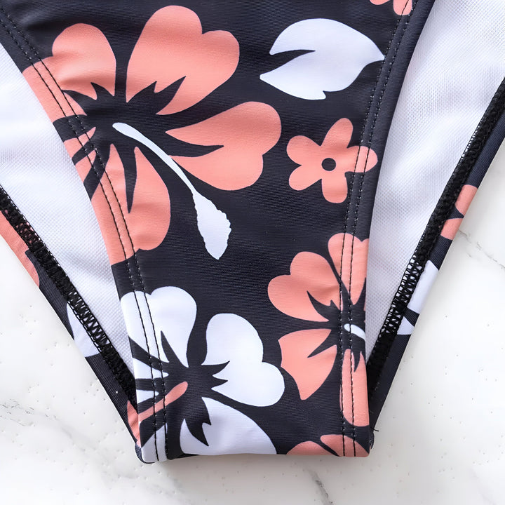 Vue arrière d'une femme portant un bikini à motif floral noir, rose et blanc. Vêtement de plage estival avec des fleurs tropicales. Style de vacances.
