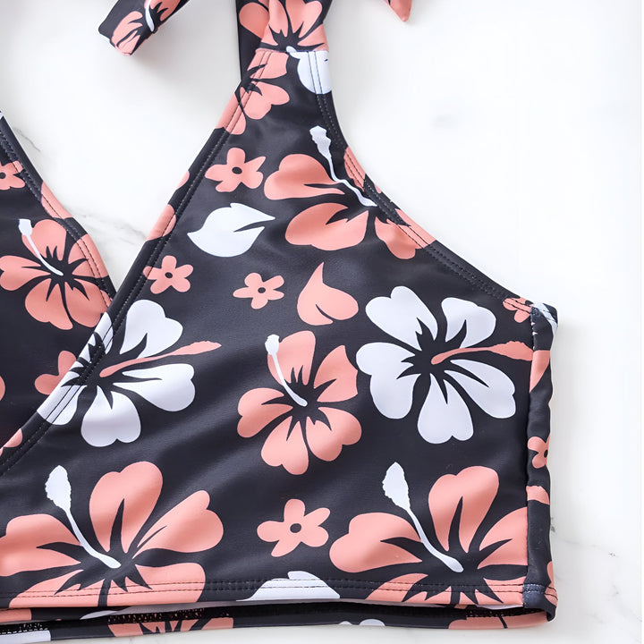 Femme en maillot de bain deux pièces noir à motifs floraux roses et blancs, chapeau de paille et veste en jean claire.