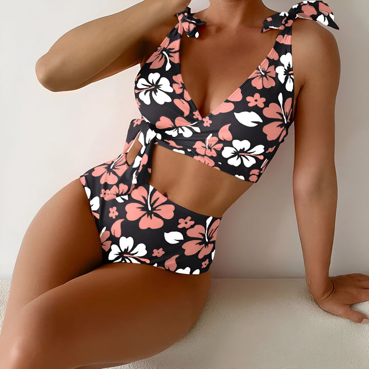 Gros plan d'une femme portant un bikini à motif floral noir, rose et blanc. Elle porte un chapeau de paille et une veste en jean ouverte. La peau bronzée est visible.