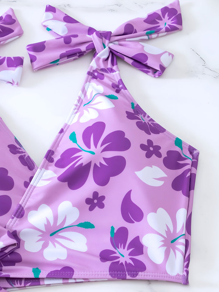 Vue arrière d'une femme portant un bikini vert à motif floral, coiffée d'un chapeau de paille, allongée sur un lit.