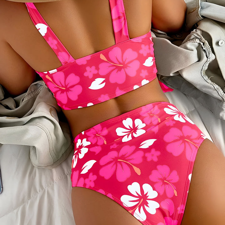 Vue arrière d'une femme en maillot de bain deux pièces orange à motif floral rouge et blanc, allongée sur un lit avec une veste en jean à côté. Mode estivale, vêtements de plage, ambiance tropicale.