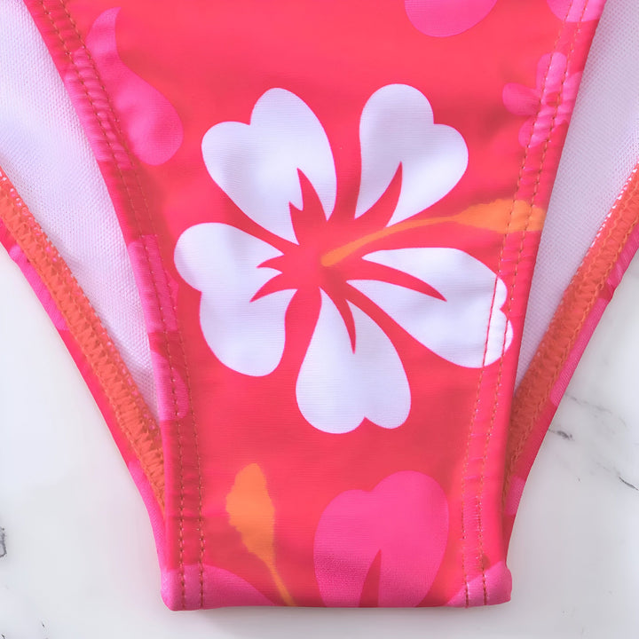 Femme allongée en maillot de bain deux pièces orange à motifs floraux, portant un chapeau de paille et une veste en jean. Mode été, vacances, tenue de plage.