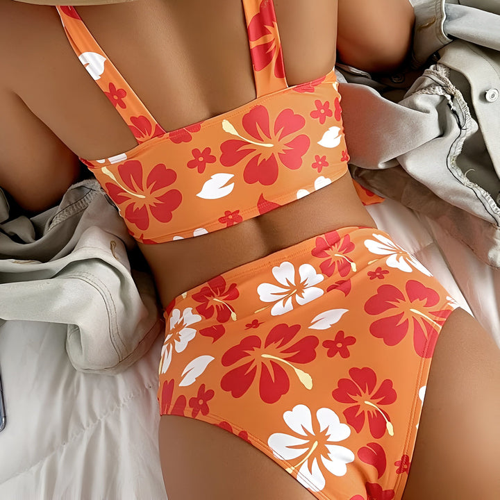 Vue arrière d'une femme portant un bikini rose vif à imprimé floral blanc, allongée sur un lit avec une veste en jean clair à côté d'elle. La lumière naturelle met en valeur les détails du maillot de bain et la texture du tissu.