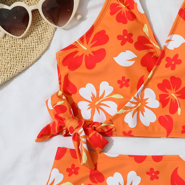 Femme en maillot de bain deux pièces rose à fleurs, chapeau de paille et veste en jean claire, allongée sur un lit. Mode estivale, vacances à la plage.