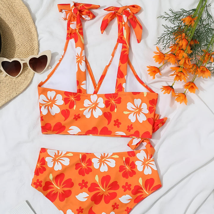 Femme portant un maillot de bain deux pièces lilas à motif floral. Haut avec bretelles à nœuds, bas taille haute à nouer sur le côté. Style estival et tendance.