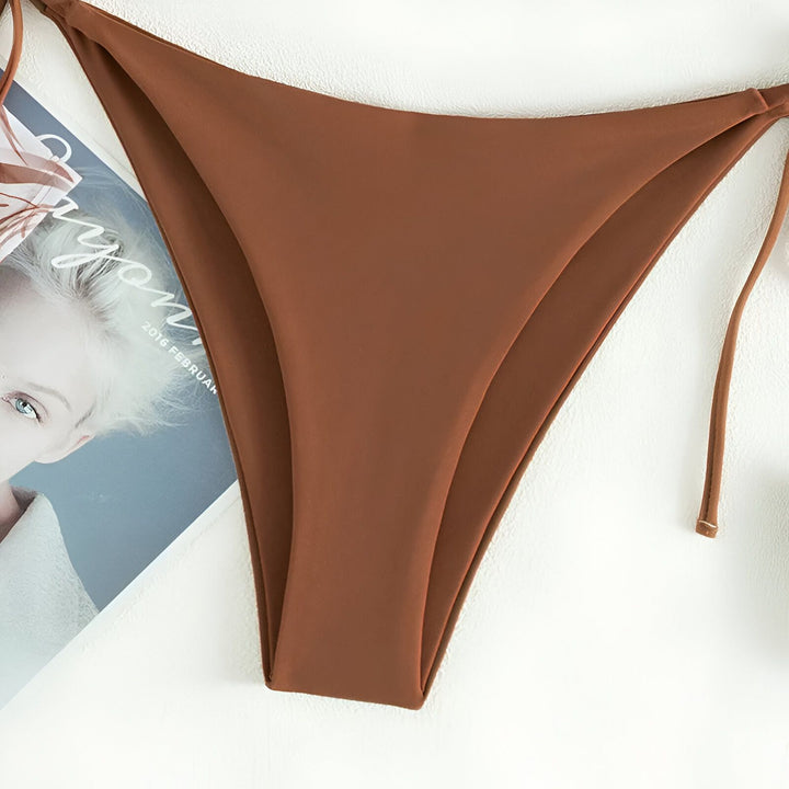 Culotte de bikini marron avec attaches latérales, posée sur un magazine de mode sur fond blanc. Mode balnéaire, été, maillot de bain.