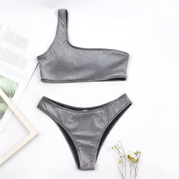 Ensemble de bikini doré une épaule sur fond rose avec feuille de palmier et bracelets. Maillot de bain tendance pour l'été.