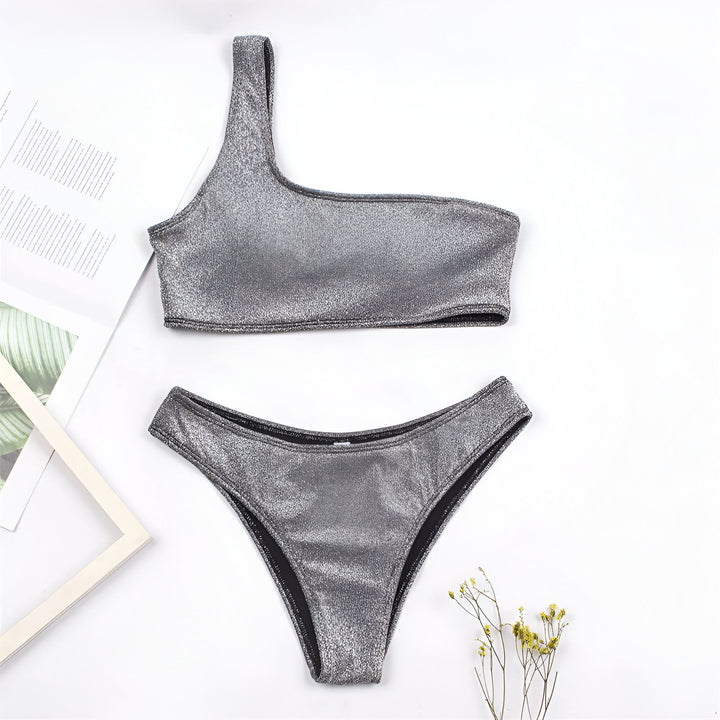 Ensemble de bikini doré une épaule sur fond rose avec feuille de palmier et bracelets. Maillot de bain tendance pour l'été.