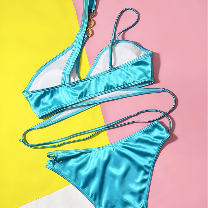 Gros plan d'une femme portant un bikini turquoise brillant avec des détails dorés, accessoirisée d'un chapeau de paille et d'une veste en jean. Détails sophistiqués et look estival tendance.