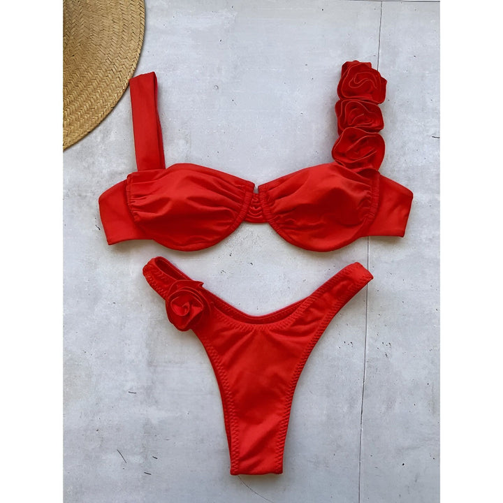 Image d'une femme portant un bikini noir avec des ornements floraux. Haut de bikini bandeau froncé et bas de bikini échancré avec détail de fleur assorti. Look élégant et estival pour la plage ou la piscine.