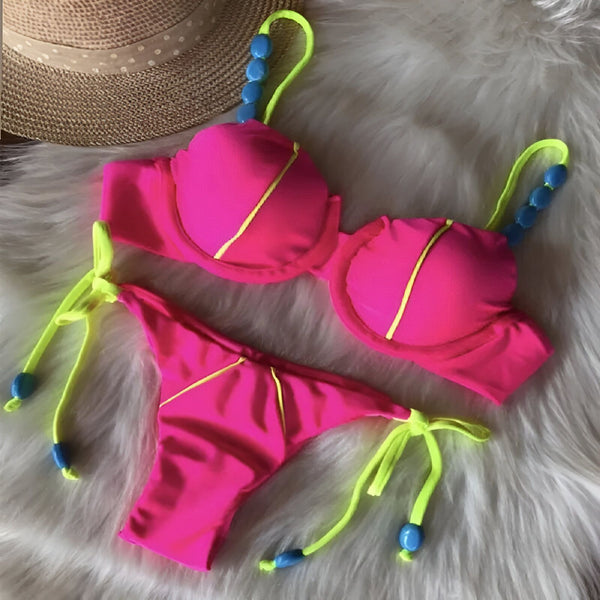 Ensemble de bikini jaune fluo et rose fuchsia sur un fond en bois avec un sac de plage en paille. Le maillot de bain deux pièces a des bretelles décorées de perles bleues. Idéal pour l'été et les vacances à la plage.