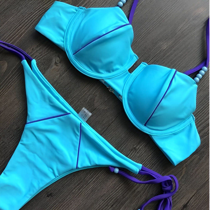 Vue rapprochée d'un ensemble de bikini rose vif et blanc avec des détails jaune néon sur une surface sombre à motifs de marbre. Le soutien-gorge a des bonnets rembourrés et des bretelles réglables. La culotte de bikini a des cordons latéraux.