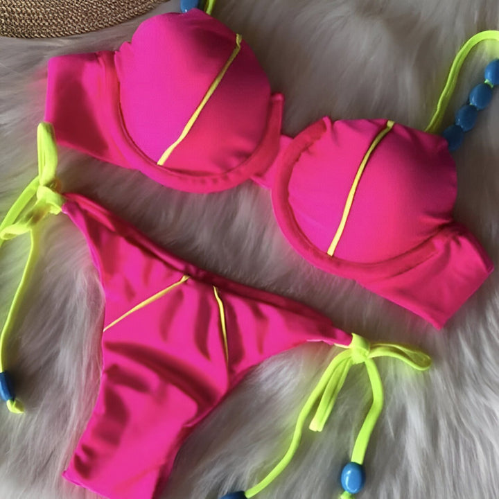 Image d'un ensemble de bikini rose vif avec des détails jaune fluo sur un fond en marbre noir. Le bikini est composé d'un haut de soutien-gorge et d'une culotte assortie, idéaux pour l'été.
