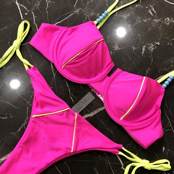 Image d'un bikini rose vif avec des détails jaune fluo, mis en valeur sur un fond de fausse fourrure blanche. Le soutien-gorge est à armatures et le bas est noué sur les côtés, agrémenté de perles bleues. Idéal pour un look estival audacieux.