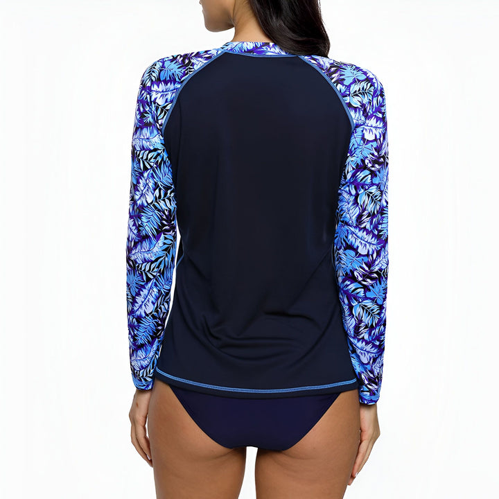 Femme portant un ensemble de bain deux pièces bleu marine avec un haut à manches longues imprimé de feuilles bleues et violettes. Tenue de plage tendance et confortable. Vêtements de bain pour femme.