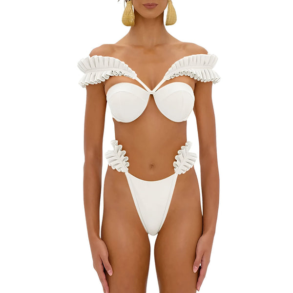 Une femme porte un maillot de bain vert émeraude avec des volants. Haut de bikini bandeau avec un lien au centre. Le bas est taille haute. Le fond est blanc. Mode de plage.